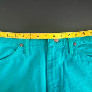 May include: Teal blue denim jeans with a yellow measuring tape across the waistband. The tape reads 1 through 15.