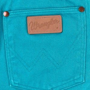 May include: A close-up of a turquoise blue pair of jeans with a brown leather patch that says "Wrangler" on the back pocket.