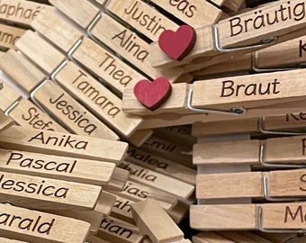May include: A close-up of wooden clothespins with names written on them. The clothespins are decorated with red hearts. The names include: Andreas, Anette, Rene, Alp, Braeuti, Braut, Justin, Alina, Thea, Tamara, Jessica, Sternika, Pascal, Jessica, Arald, in, h, Rolph, Martina, Emil, Malea, ulia, jas, ah, tian, Den, Maliya, Luca, lia.