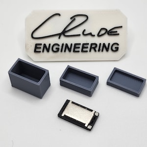 May include: Three gray plastic boxes and a small black speaker component. The boxes are rectangular and have a slightly textured surface. The speaker component has a silver metal diaphragm.