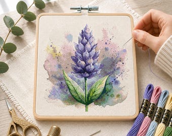 May include: A square wooden embroidery hoop containing a fabric panel with a cross-stitch design of a purple lavender flower. The design features watercolor-style splashes in shades of pink, blue, and yellow. Embroidery floss, scissors, and a thimble.