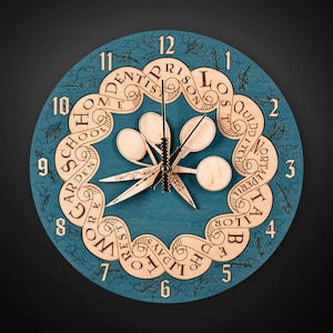 Puede incluir: Un reloj redondo de madera de color turquesa con un dise&ntilde;o &uacute;nico. La esfera del reloj presenta un borde decorativo con motivos de hojas y palabras como "HOME", "SCHOOL" y "WORK". Las manecillas y el centro del reloj son de madera clara.
