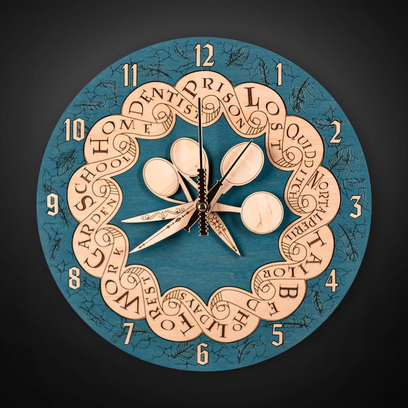 Puede incluir: Un reloj redondo de madera de color turquesa con un dise&ntilde;o &uacute;nico. La esfera del reloj presenta un borde decorativo con motivos de hojas y palabras como "HOME", "SCHOOL" y "WORK". Las manecillas y el centro del reloj son de madera clara.