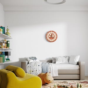 Puede incluir: Una habitaci&oacute;n infantil con un reloj de pared redondo con un dise&ntilde;o floral, un sill&oacute;n amarillo, un juguete con forma de hipop&oacute;tamo y un juego de trenes de madera sobre una alfombra estampada. Un sof&aacute; cama est&aacute; en el fondo.