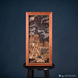May include: A wooden wall clock with a layered design depicting a castle scene under a night sky. The clock has Roman numerals and gold-colored hands, set within a rectangular, brown wooden frame. The clock is sitting on a black stool.