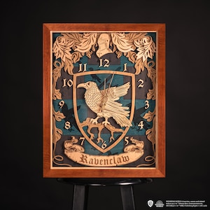 Può includere: Un orologio da parete in legno con lo stemma della casa Ravenclaw della serie Harry Potter. L'orologio ha uno sfondo blu e verde con un corvo e le parole "Ravenclaw" in uno stendardo.