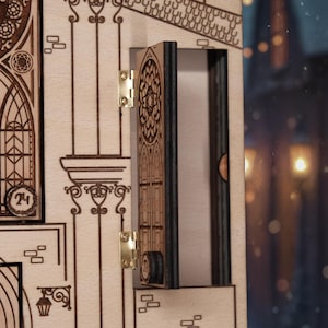 Op de afbeelding: Een houten adventskalender met een open deur die een compartiment onthult. De kalender heeft ingewikkelde lasergesneden ontwerpen van architecturale elementen, waaronder boogvensters en decoratieve kolommen. De deur is bevestigd met messing scharnieren.