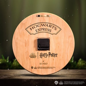 K&ouml;nnte beinhalten: Eine runde Holzuhr mit dem Hogwarts Express Logo, dem Text Harry Potter und dem Logo der Zaubererwelt. Die Uhr ist aus Holz und hat ein schwarzes Zifferblatt.