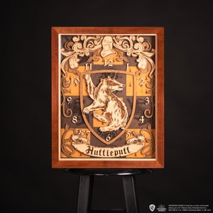 Può includere: Un orologio in legno con lo stemma della casa Tassorosso della serie Harry Potter. L'orologio ha la forma di uno scudo con un tasso al centro. Il quadrante dell'orologio è circondato da una cornice decorativa con le parole "Tassorosso" scritte sotto.