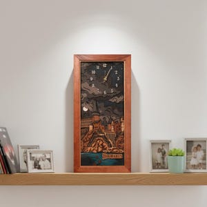 May include: A rectangular wooden clock with a brown frame. The clock face features a layered design depicting a castle scene with a dark sky, moon, and the word "Hogwarts" at the bottom. The clock hands show the time.