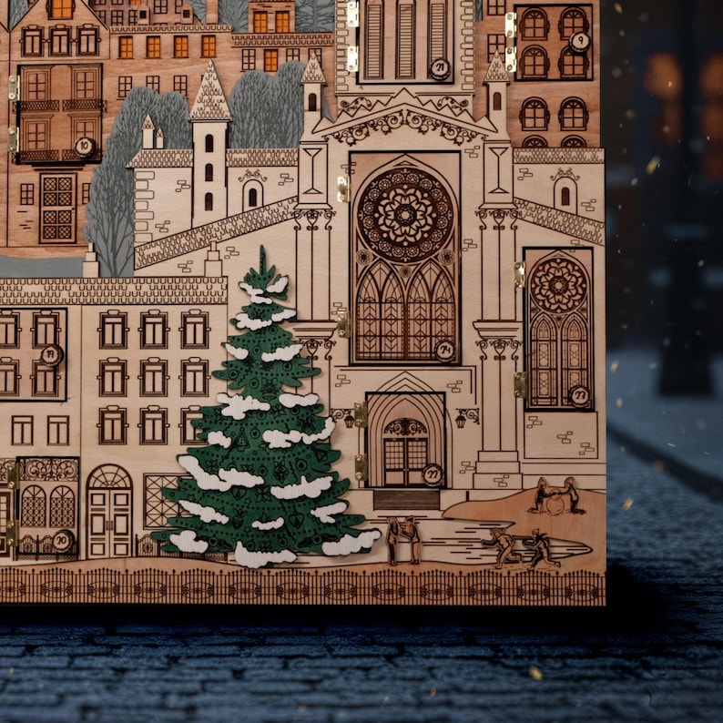 Op de afbeelding: Een houten adventskalender met een gedetailleerd stadsgezichtontwerp. De kalender heeft een groene kerstboom met witte accenten, gebouwen en een kerk. Het ontwerp is lasergesneden.