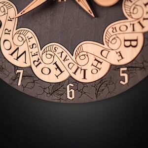 Puede incluir: Primer plano de una esfera de reloj de madera con fondo gris oscuro. El reloj presenta n&uacute;meros y texto decorativo cortados con l&aacute;ser, incluyendo las palabras "WORK", "REST", "HOLIDAY" y "BED". Las manecillas del reloj son visibles en la parte superior.