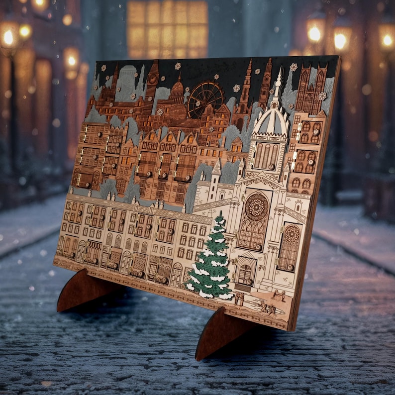 Op de afbeelding: Houten adventskalender met een gedetailleerd stadsgezichtontwerp. Het lasergesneden kunstwerk toont gebouwen, een reuzenrad en een kerk, met een kleine groene kerstboom. De kalender staat op een houten standaard.