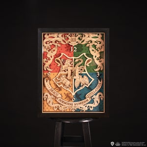 Può includere: Un orologio da parete in legno con gli stemmi delle case di Hogwarts. L'orologio è incorniciato in nero e presenta un design dettagliato con le mascotte delle case e i motti latini. Il quadrante dell'orologio è diviso in quattro sezioni, ciascuna rappresentante una casa diversa: Grifondoro, Tassorosso, Serpeverde e Corvonero.