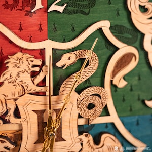 May include: A wooden clock featuring the Hogwarts house crests. The clock face is made of wood and features a lion, snake, badger, and eagle. The clock hands are gold.