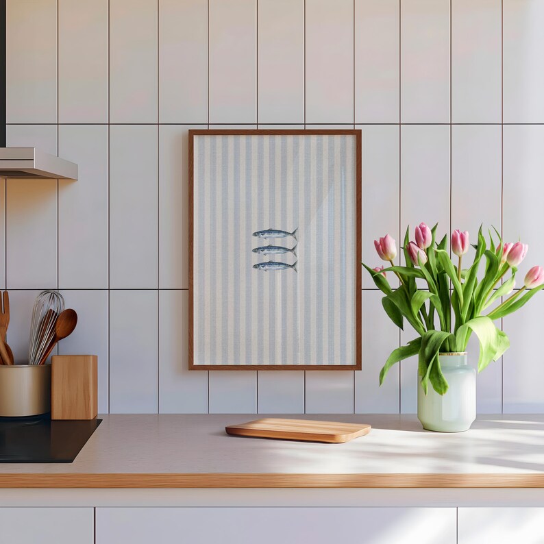 K&ouml;nnte beinhalten: Ein rechteckiger Wandkunstdruck in einem braunen Rahmen mit einem vertikal gestreiften hellblauen und wei&szlig;en Hintergrund und drei kleinen, horizontal ausgerichteten Fischillustrationen in der Mitte der Komposition.