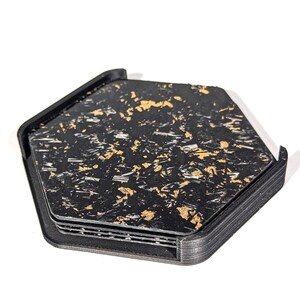 May include: A set of four black hexagonal coasters with a gold flecked pattern. The coasters are stacked on top of each other.