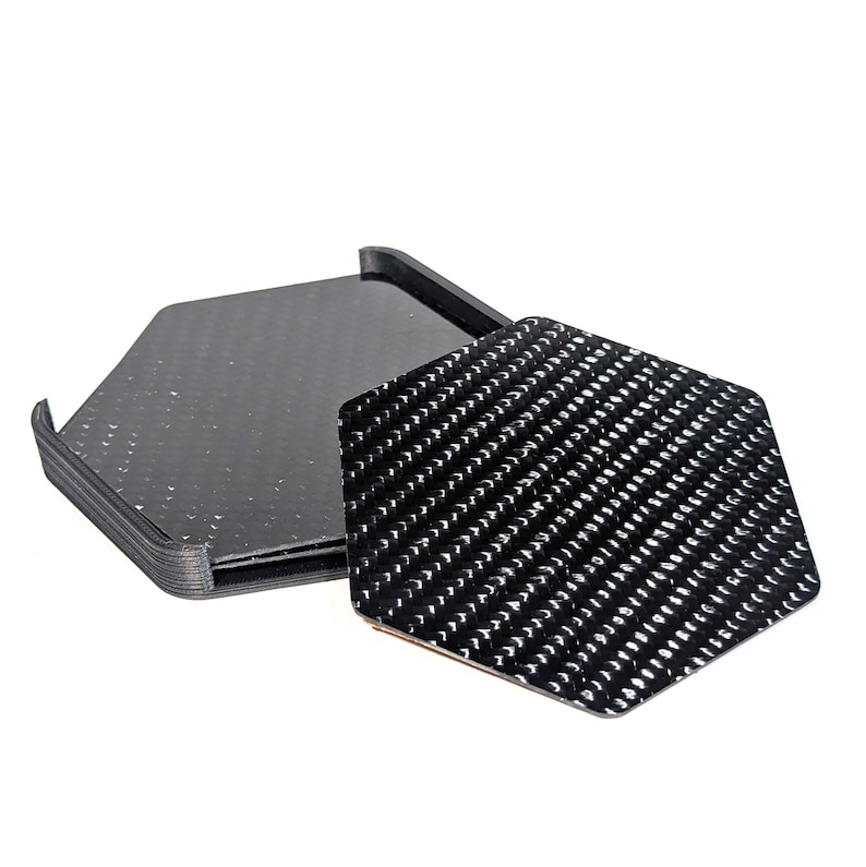 May include: Set of six black hexagonal coasters with a carbon fiber pattern. The coasters are made of a durable material and are perfect for protecting your furniture from scratches and spills.