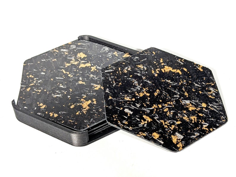 May include: A set of six black and gold hexagonal coasters with a geometric pattern. The coasters are made of a composite material and are designed to protect surfaces from scratches and heat.