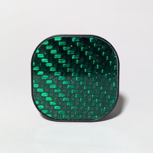 May include: A green and black square-shaped phone grip with a carbon fiber pattern.