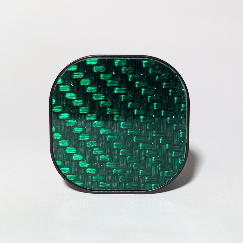 May include: A green and black square-shaped phone grip with a carbon fiber pattern.