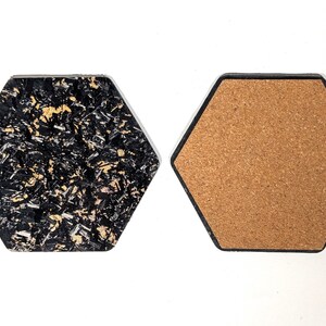 May include: Two hexagonal coasters, one with a black and gold speckled surface and the other with a brown cork surface.