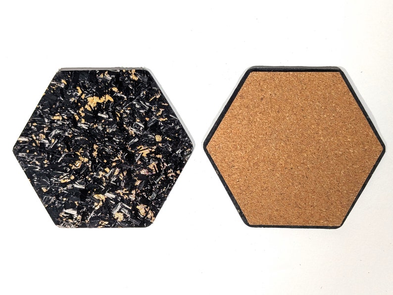 May include: Two hexagonal coasters, one with a black and gold speckled surface and the other with a brown cork surface.