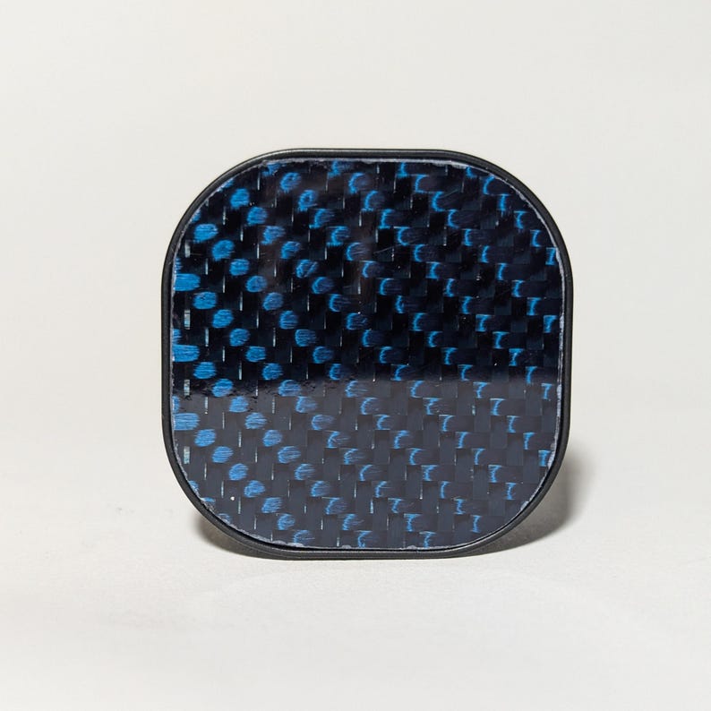 May include: A black square-shaped button with a blue and black carbon fiber pattern.