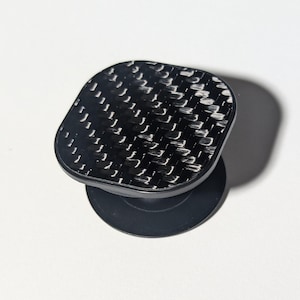 May include: A black phone grip with a carbon fiber pattern.