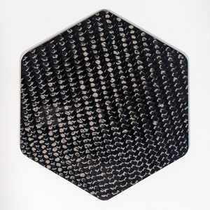 May include: A black hexagonal piece of carbon fiber material with a woven pattern.