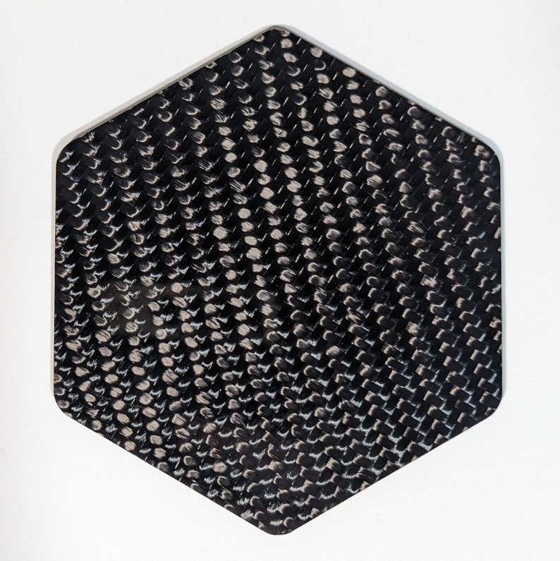 May include: A black hexagonal piece of carbon fiber material with a woven pattern.