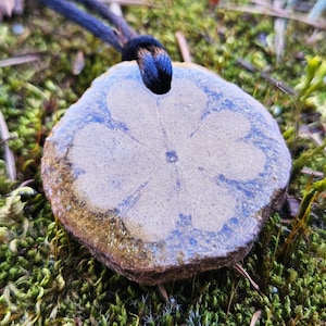 May include: A brown and white ceramic pendant shaped like a flower with a blue center. The pendant is hanging from a black cord.