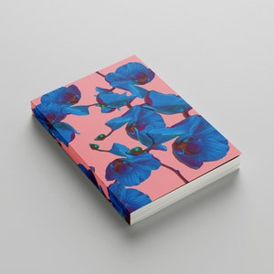 Könnte beinhalten: Ein rosa Notizbuch mit einem blauen Orchideen-Blumenmuster auf dem Einband.