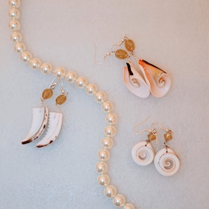 May include: A white pearl necklace with three pairs of shell earrings. The earrings are made with different types of shells and have gold accents.