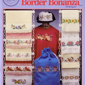 May include: A cross stitch pattern book titled "Border Bonanza" with 50 designs. The book cover features a variety of cross stitch designs on towels, a hat, a bag, and a sweater. The designs include flowers, birds, butterflies, and other motifs.