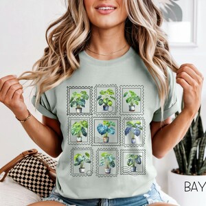 Puede incluir: Una camiseta verde claro con un diseño de nueve sellos postales, cada uno con una ilustración de una planta en maceta. Las plantas tienen hojas verdes y están en varias macetas. La camiseta tiene mangas cortas y cuello redondo.