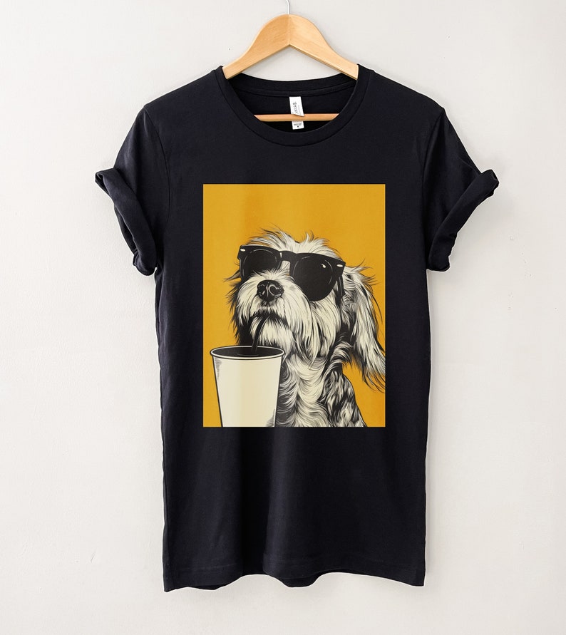 May include: Black t-shirt with a graphic of a dog wearing sunglasses and drinking from a cup with a straw. The dog is on a yellow background.