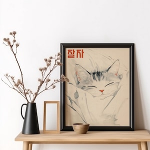 May include: A black framed print of a cat sleeping in a white blanket. The print has the Korean word "잠자" in red lettering at the top.