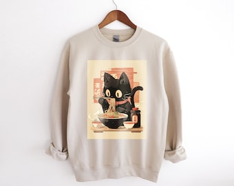 May include: A beige sweatshirt with a black cat eating ramen noodles. The cat is wearing a red scarf and is holding chopsticks. The ramen bowl is on a wooden table with a small plate of food and a bottle of soy sauce. The text "天婦羅" is written in Japanese on the wall behind the cat.
