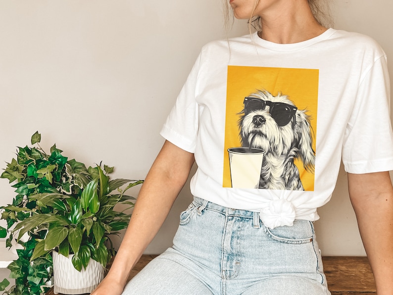 May include: White t-shirt with a graphic of a dog wearing sunglasses and drinking from a cup. The dog is on a yellow background.