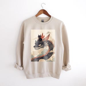 Gato negro de dibujos animados montando una sudadera de dragón / Suéter de fantasía acogedor / Regalo de amante de los gatos Kawaii / Diseño de gato cálido y divertido / Ropa casual de anime
