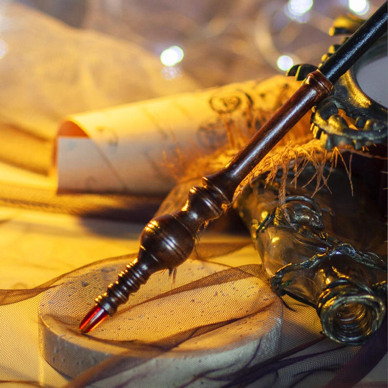 May include: A handcrafted wooden wand with a dark brown finish and a red tip, resting on a circular stone surface. The wand is detailed with carved patterns. A scroll and a decorative bottle are in the background.