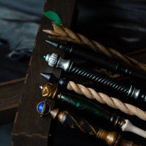 May include: A set of five wooden wands with different colored tips and decorative details. The wands are arranged in a wooden box.