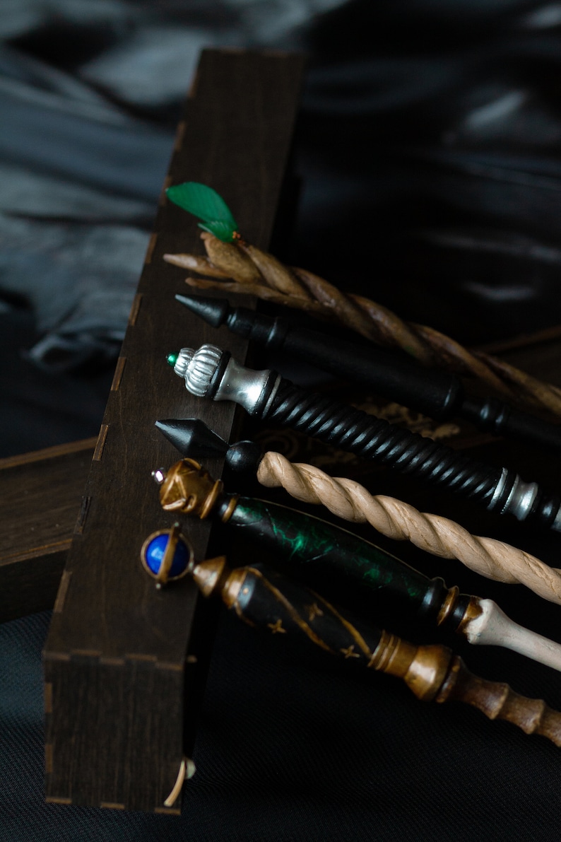 May include: A set of five wooden wands with different colored tips and decorative details. The wands are arranged in a wooden box.