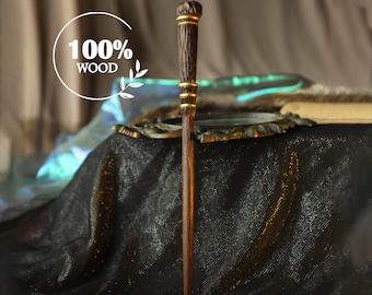 May include: A handcrafted wooden wand with a dark brown finish, accented with gold-colored bands. The wand features a textured handle and a slender, tapered design. The text "100% WOOD" is displayed in a white circle.