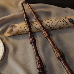 May include: Three wooden wands with intricate carvings, lying on a brown fabric surface with a rolled up piece of paper with handwritten text.