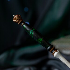 May include: A black and green wand with a brown and silver top. The wand has a detailed design with green accents.