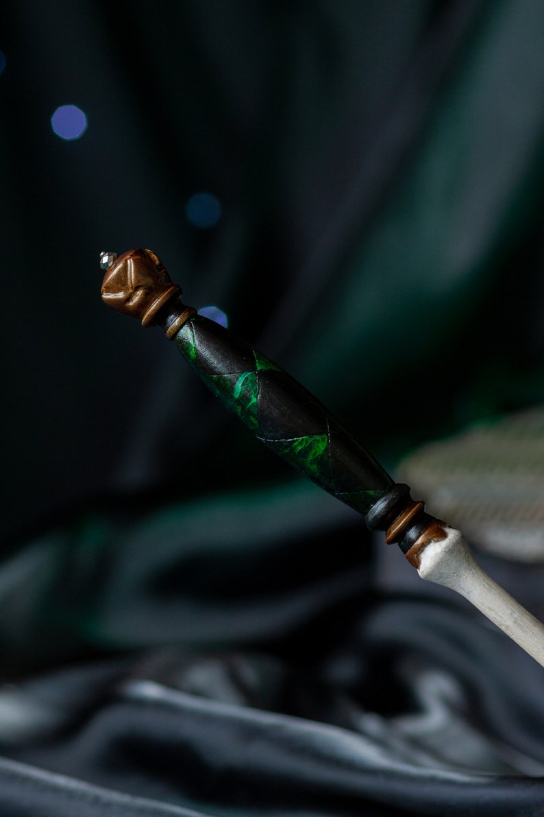 May include: A black and green wand with a brown and silver top. The wand has a detailed design with green accents.
