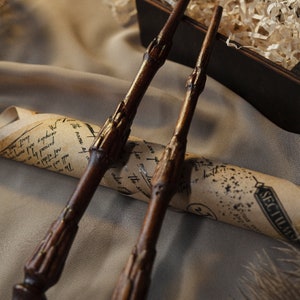 May include: Two wooden wands with gold accents, lying on a rolled up piece of parchment paper with handwritten text that reads "The name of a complex perused by an", "sove you", "The sam", "also", "will and", "Last mat", and "SECTUMN".