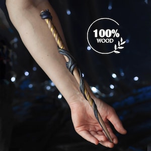 Könnte beinhalten: Ein Zauberstab aus Holz mit einem dunkelgrauen und goldenen Design. Der Zauberstab wird in der Hand einer Person gehalten. 100% Holz.